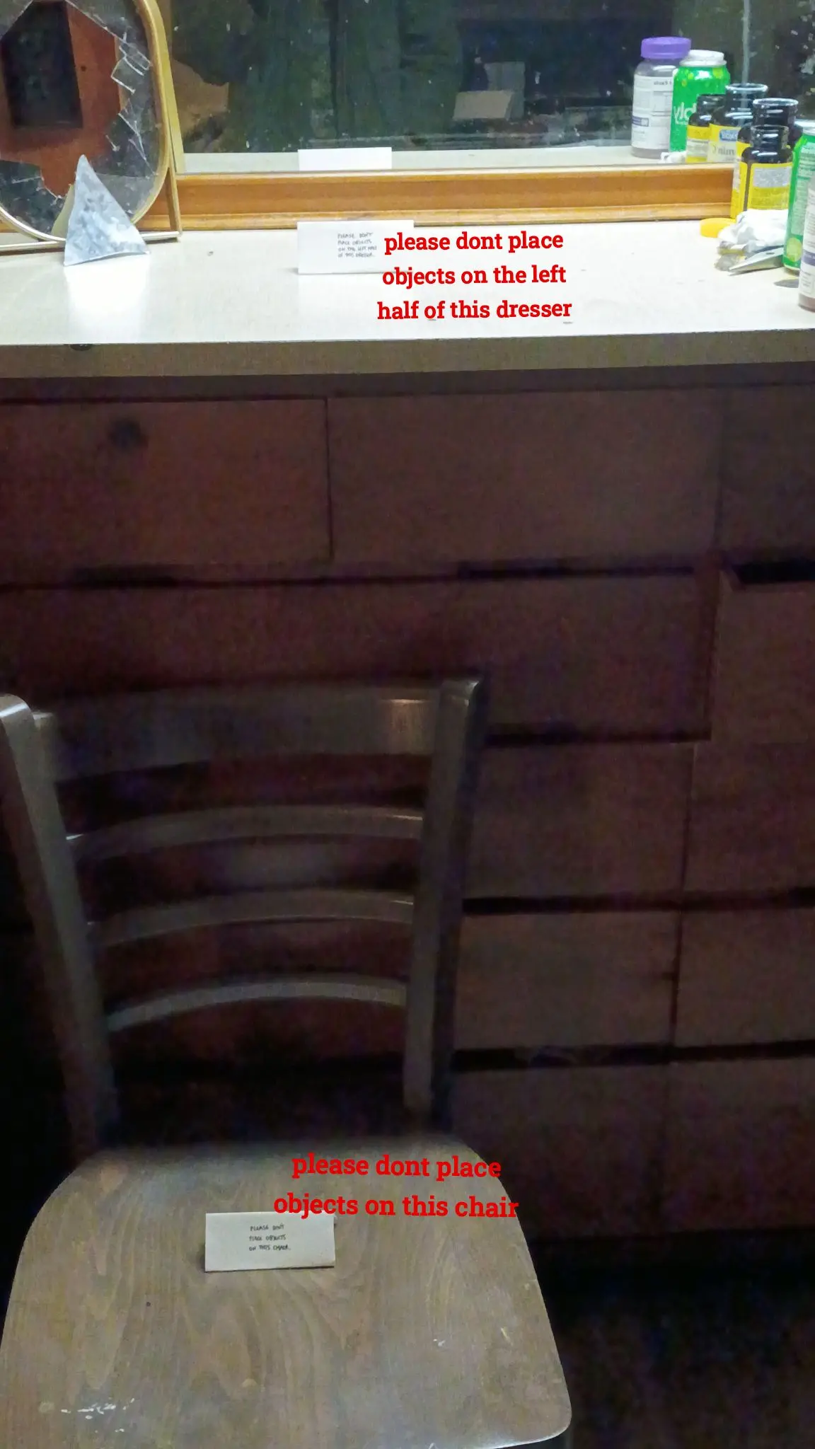 a chair with a sign that says "please dont place objects on this chair". there is a dresser with a sign that says "please dont place objects on the left half of this dresser. there are some multivitamins barely visible on the right half of the dresser.